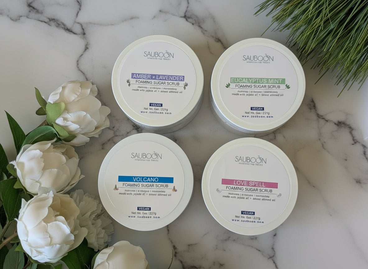 Four containers of Sauboon foaming sugar scrub on a marble surface with flowers and greenery.